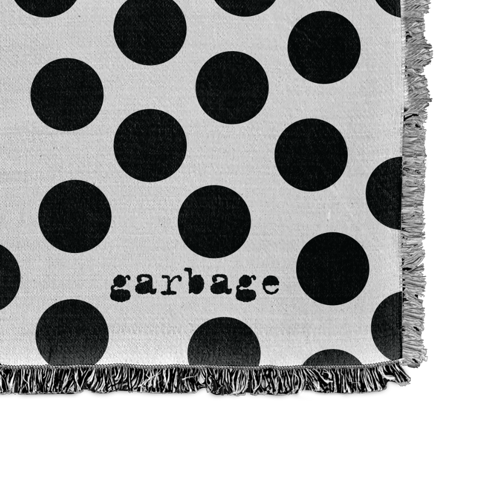 Polka-dotted fabric or textile with the word ’garbage’ printed on it and fringed edges.